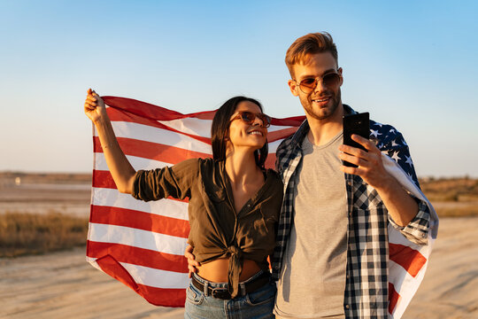Nice happy couple using cellphone while strolling with american flag - Powered by Adobe