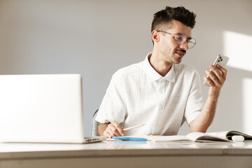 Photo of focused man using mobile phone while working with laptop