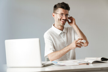 Photo of smiling unshaven man using earphones working with laptop