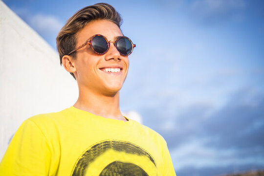 Portrait of handsome young guy boy smiling with sun in front - outdoor leisure activity and happy beautiful people with sunglasses, yellow and blue color backgorund