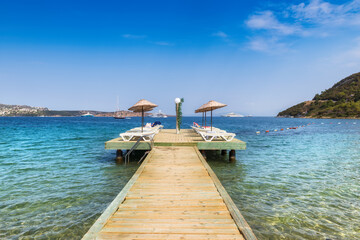 Beach pier with sun umbrellas and beach loungers in Aegean sea, Golturkbuku beach, Bodrum, Turkey.