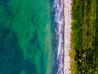 Top down aerial view of a sandy beach in the summer with waves crashing ashore.