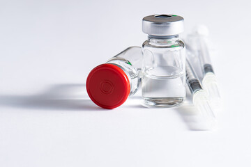 Glass vials with transparent liquid and plastic syringes on white background close up. Season...