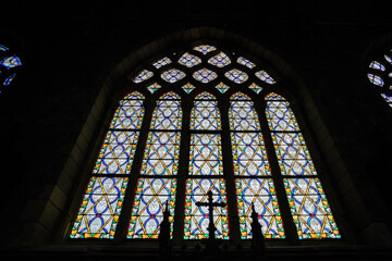 Stained glass window in a church with a cross in the foreground.