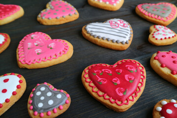 Heart shaped with cute royal icing pattern cookies scattered on black wooden background