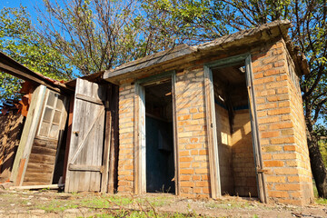 abandoned old brick toilet with two doors at sunny summer day.