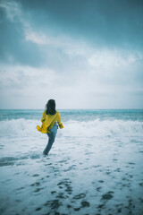 ragazza con maglia gialla e jeans si fa il bagno a mare in inverno