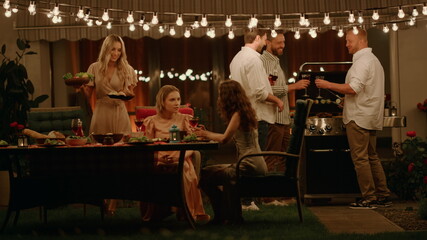 Friends enjoying barbeque party. Men preparing meat. Women talking at table - obrazy, fototapety, plakaty