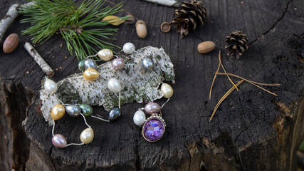 Multicolored natural large pearl necklace and a purple sparkling crystal lie on a dark stump among...