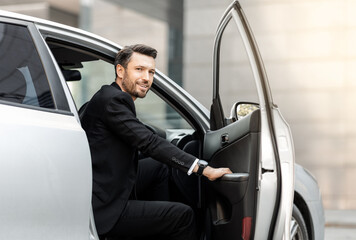 Fototapeta na wymiar Smiling bearded businessman getting in a car