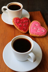 Two cups of coffee with lovely heart shaped royal icing cookies on wooden background