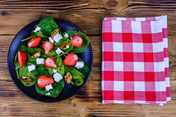 Salad with spinach leaves, feta cheese, walnuts and strawberry on a black plate. Top view