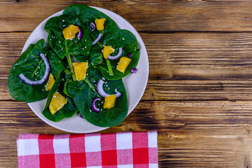 Salad with spinach leaves, pieces of orange, sesame seeds and onion in a ceramic plate. Top view