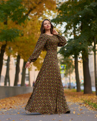 Elegant caucasian brunette woman with long wavy hair in long brown dress with floral print walking...