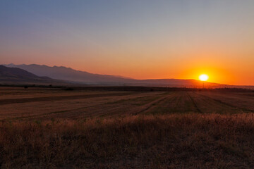 Fototapeta na wymiar Sunset in the mountains. Autumn field in the foreground and mountains against the backdrop of the red sky and the setting sun. Kyrgyzstan.