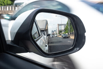 Side view mirror from a white car waiting for a traffic light, reflection of coming cars on the urban highway during morning time.