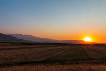 Sunset in the mountains. Autumn field in the foreground and mountains against the backdrop of the red sky and the setting sun. Kyrgyzstan.