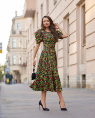 Elegant caucasian brunette woman with long wavy hair in midi green dress with floral print walking...