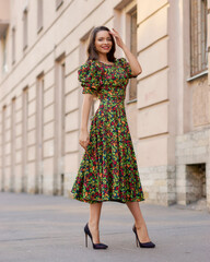 Elegant caucasian brunette woman with long wavy hair in midi green dress with floral print walking...
