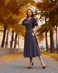 Elegant caucasian brunette woman with long wavy hair in midi purple dress with floral print walking...