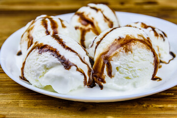 Plate with ice cream balls and chocolate topping on a wooden table