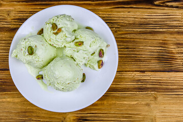 Glass bowl with pistachio ice cream balls and nuts on a wooden table. Top view
