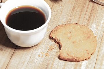 Cup of black coffee with a biscuit on a wood background