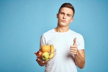 Happy man with fresh fruits gesturing with hands blue background white t-shirt vitamins bananas oranges apples