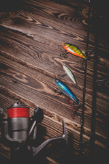 Studio photo of fishing tackle on a wooden background. A rod, a reel with a line and three wobblers.