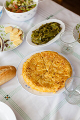 Vertical shot of home made spanish omelette plate served on a home table with green peppers and sliced cheese. Tapas at home concept.