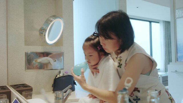 A young Asian mother helps her daughter wash her nose or rinse her nasal cavity with saline solution to prevent allergic reactions.