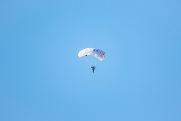 one parachutist floats slowly at low altitude on the background of clear sky