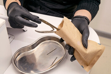 Close-up shot of a master in black gloves opening a package for sterilization of manicure tools