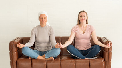 Breast cancer mother and pretty daughter sitting on couch doing meditation.