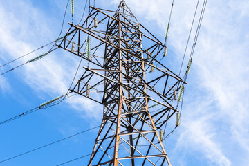 metal support of a high-voltage power line with wires and insulators against a blue sky with clouds