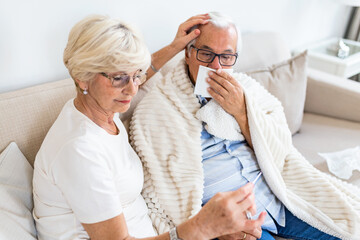 An older woman helps a ill husband while they are sitting on the couch in the living room. Senior man with flu and running nose. - Powered by Adobe