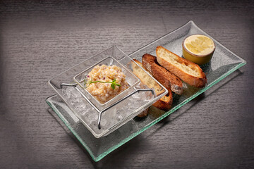 Pike fish caviar, on ice, with croutons and butter, on a transparent dish, on a dark background