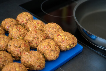 Frikadellen Gemüse Fleisch Paddys mit Kurkuma, Paprika, Linsen, Sesam und Chia Samen beim Anbraten in einer schwarzen Teflonpfanne mit Kokosöl, Produktbild	