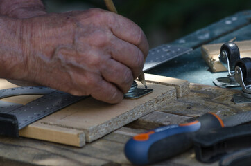 Hand of an elderly man who makes a trace on a piece of wood to install wheels