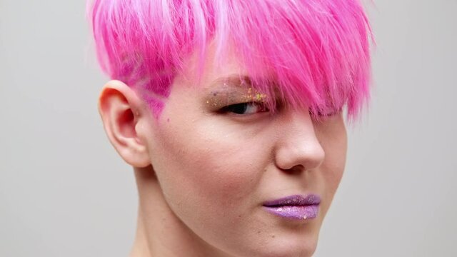 Young beautiful girl with a short haircut and pink hair. A homosexual lesbian model poses on a white background in the studio.