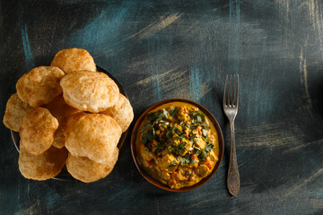 Delicious indian food curry in brown dish with bengali puff flatbread luchi on wooden table top view with copy space