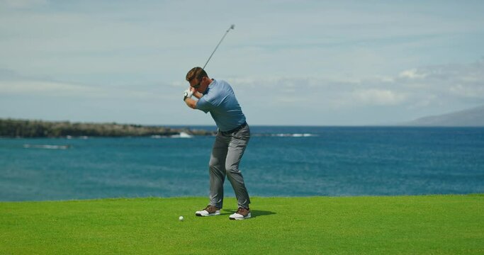 Golfer swinging and hitting golf ball on beautiful course by the ocean, slow motion