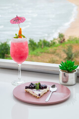 Pink mocktail on white counter bar with blueberry cheesecake.