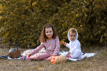 two little children, girls, sisters sit under a tree next to a pumpkin lantern with a glowing carved face for halloween on the background of an autumn garden, selective focus, bokeh