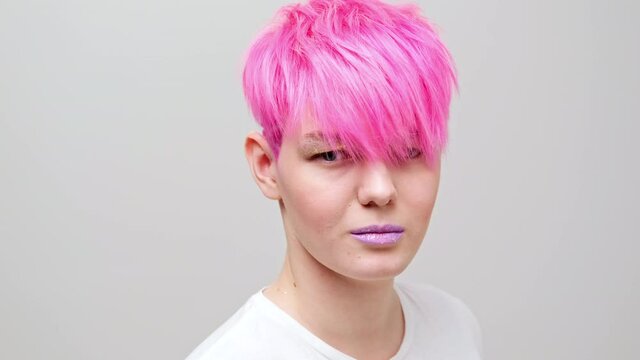 Young beautiful girl with a short haircut and pink hair. A homosexual lesbian model poses on a white background in the studio.