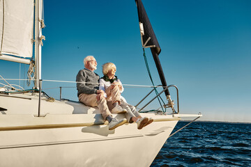 Enjoying vacation. Happy senior family couple sitting on the side of a sail boat or yacht deck...