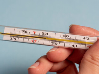 mercury thermometer in the hand of a woman isolated on a blue background. Temperature measurement using a thermometer. High fever and illness. Close up