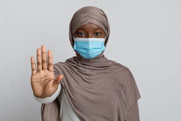 Stop Coronavirus Pandemic. Black muslim woman wearing medical mask showing stop gesture