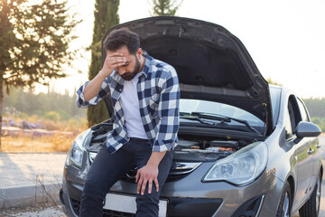 Young man with a broken car on the road