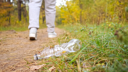 Obraz premium Unrecognizable woman throws a plastic bottle into the grass in the forest.